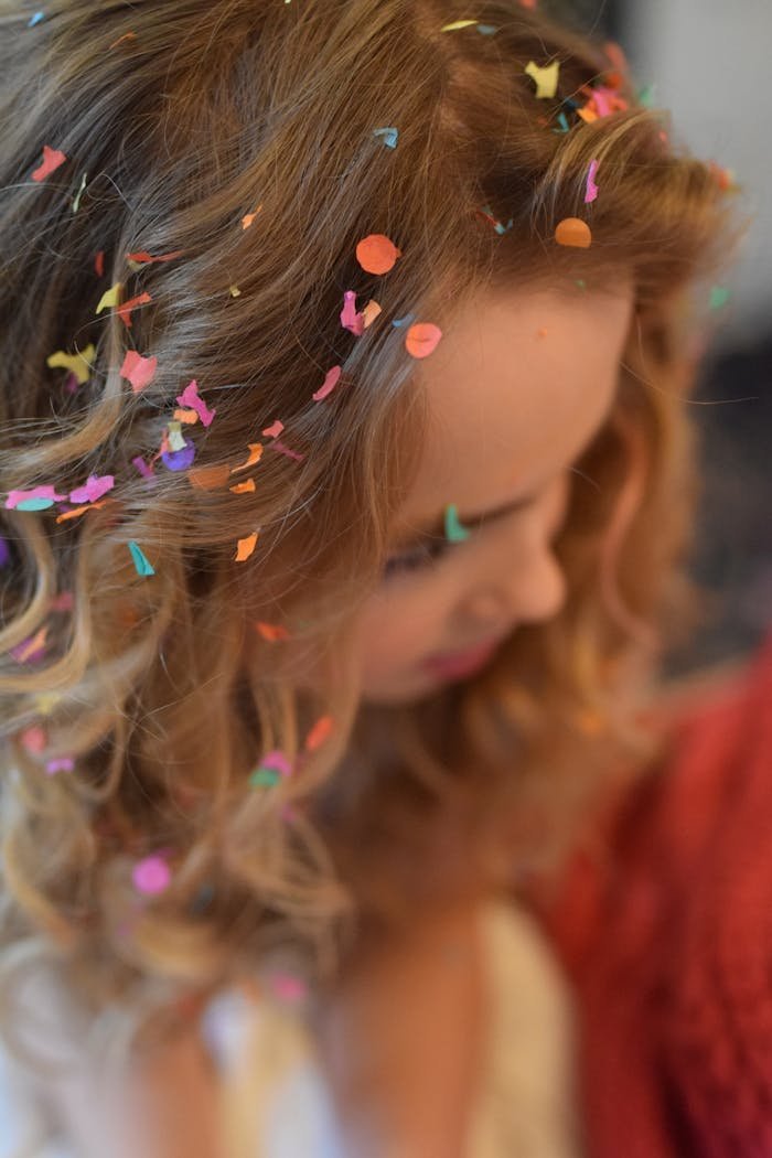 A young woman enjoying a festive moment with vibrant confetti in her hair.
